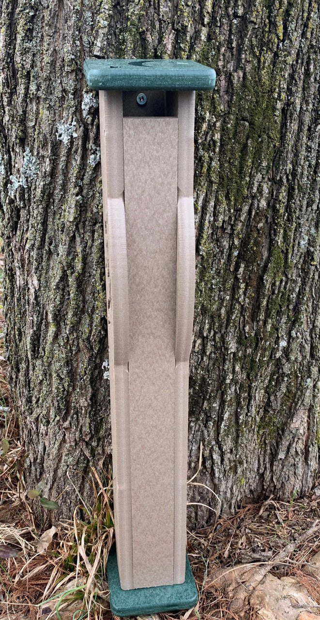 Plastic birdhouse next to a tree showing a taupe body, green top and base, and a visible screw.
