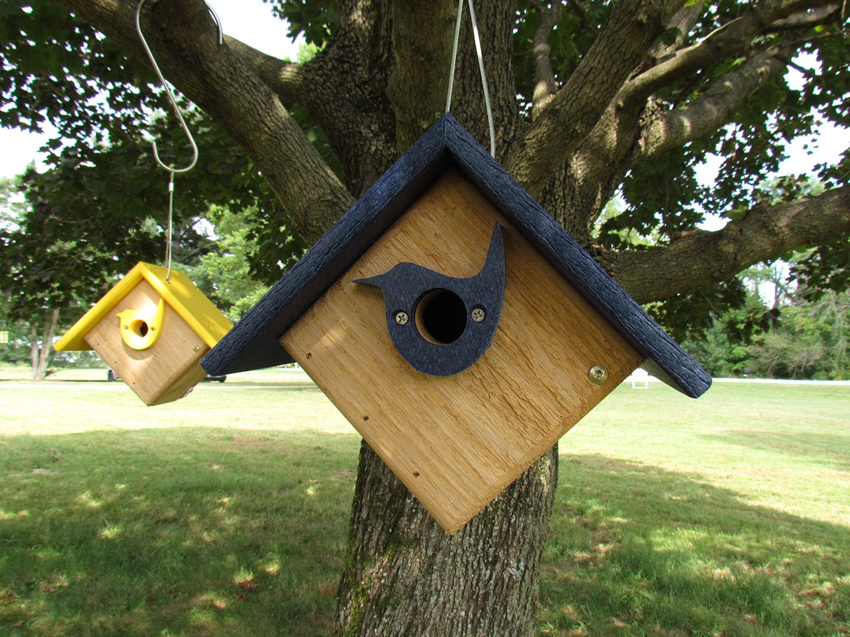 Handmade wooden birdhouses hanging from a tree in a grassy park setting featuring a dark blue roof on one house and a bright yellow roof on another with small bird-shaped cutouts