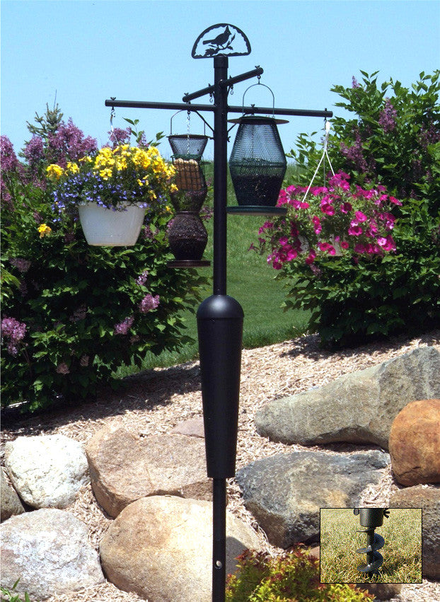 Photo of a black metal garden bird feeder with multiple hanging feeders and colorful flower baskets near large rocks and lush greenery featuring a cardinal silhouette and yellow and purple flowers

