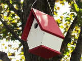 Recycled plastic birdhouse hanging from a tree showcasing a vibrant red roof white body and small entrance hole
