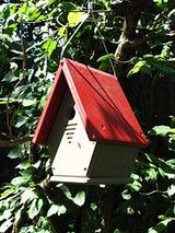 Photograph of a red and beige birdhouse hanging from a tree in a garden with vibrant green leaves and a visible tree trunk