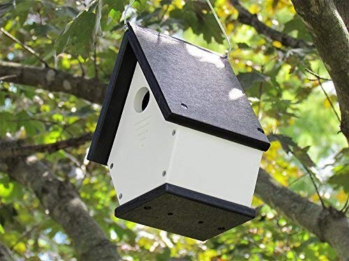 Recycled plastic birdhouse hanging from a tree branch featuring a black roof, white body, and dark grey base in a lush green garden
