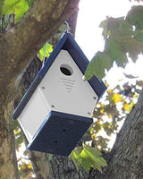 Recycled plastic birdhouse hanging from a tree branch featuring a white body, navy blue roof and base, and ventilation slots.
