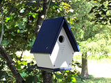 Recycled plastic birdhouse in a backyard setting features a navy blue roof and white body with ventilation slots and a small entrance hole hanging from a tree branch
