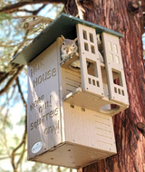Photograph of a gray squirrel in a squirrel house nesting box attached to a tree featuring a green roof, tan wood-like material, and the words Keep out! Squirrels only!
