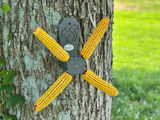 Jos Wildlife four ears of yellow corn on a gray wooden feeder attached to a tree trunk with lichen and a carved squirrel detail
