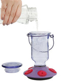 Hand pouring nectar into the Perky-Pet Lavender Field Top-Fill Glass Hummingbird Feeder 16 oz, featuring a wide-mouth opening and removable lid.